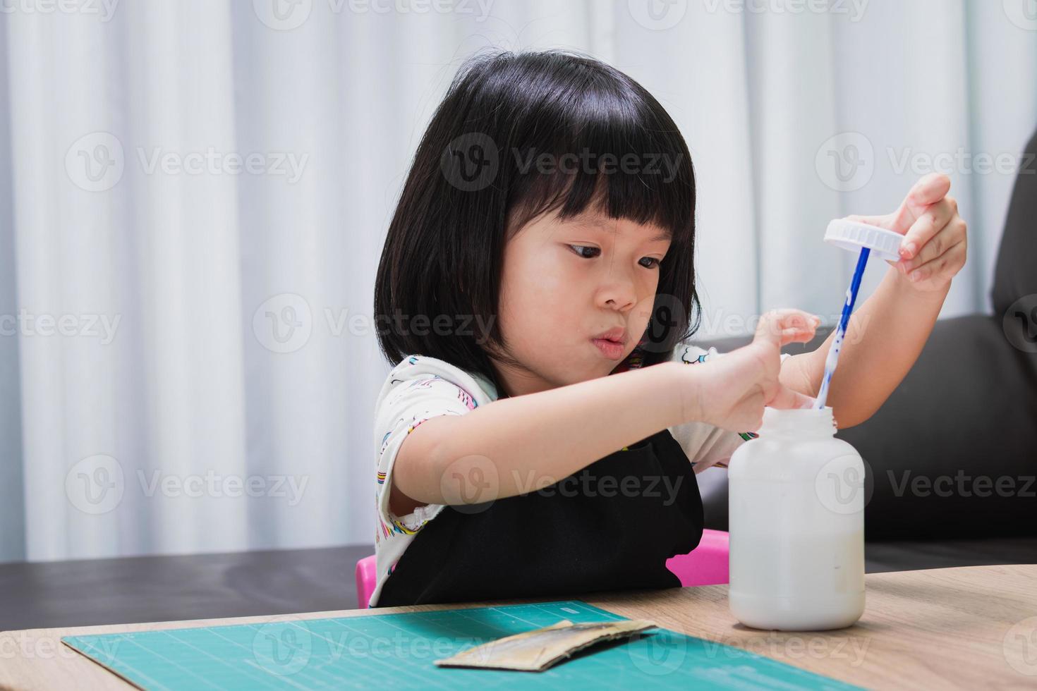 Basteln für Kinder. kreatives kind klebt werkstückdesign mit kleber. Kunst- und Kreativunterricht in Schule oder Kindergarten. Vorschulkind mit lustigem DIY-Projekt. Baby im Alter von 4-5 Jahren mit schwarzer Schürze foto