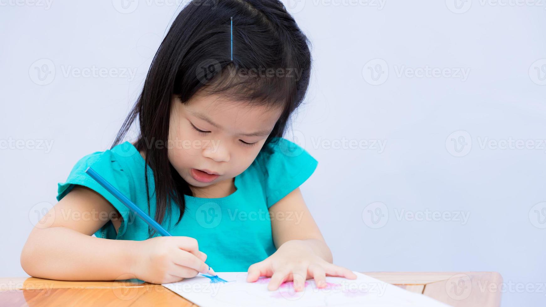 glückliches Kind mit ihrem imaginären Kunstwerk. Kinder zeichnen Kunst und Holzfärbung. süßes Mädchen, das mit der rechten Hand einen blauen Farbstift hält. Kind zeichnet auf Papier auf braunem Holztisch. 3-4 Jahre alt. foto