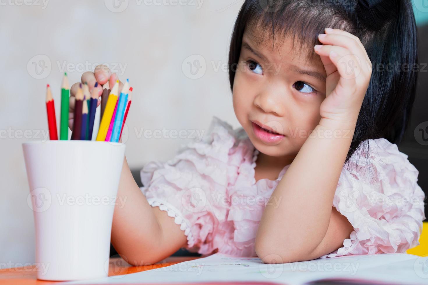 Mädchen saß und hörte zu, wie die Erwachsenen ihre Hausaufgaben machten, und sie spielte die Holzfarbe im weißen Glas. Kinder waren von den Anweisungen verwirrt. foto