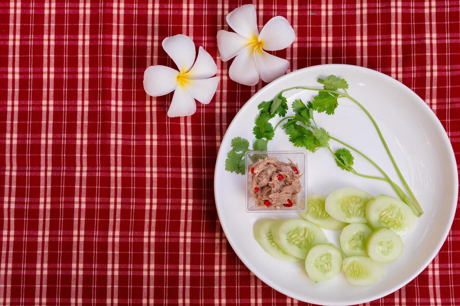 Yum Thunfischsalat ist klein auf einem weißen Teller, garniert mit Melonen und frischem grünem Koriander. roter und weißer karierter Stoffhintergrund. Vintage-Stil. mit Frangipani-Blüten verziert. foto