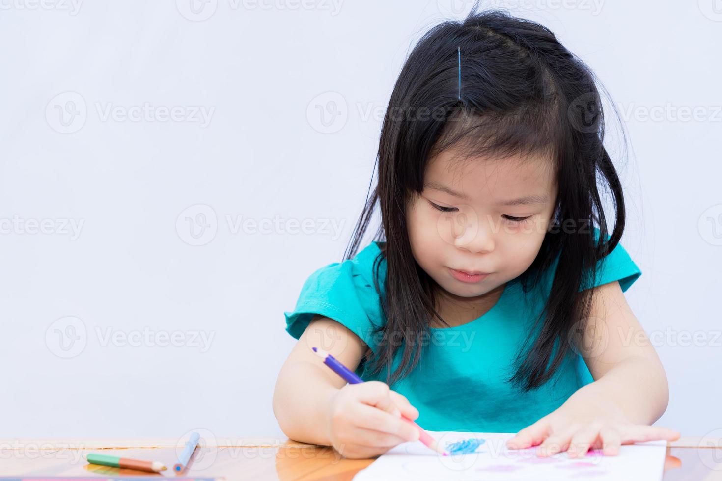 asiatisches Mädchen studiert Kunst. Kind malen mit Farbe Holz. Schüler basteln an Zeichenbüchern. Kinder tragen grüne Kleidung. schwarzhaarige Kinder genossen das Zeichnen. Baby macht Hausaufgaben auf Holztisch. foto