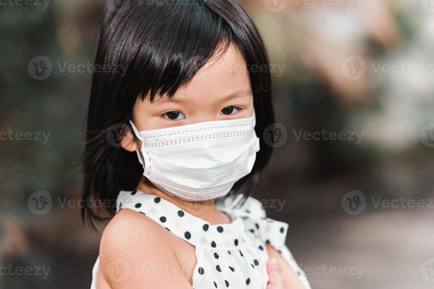 Nahaufnahme des Gesichts eines süßen Mädchens, das eine medizinische weiße Gesichtsmaske trägt, um die Ausbreitung des Coronavirus Covid-19 und PM2.5-Staubpartikel zu verhindern. foto