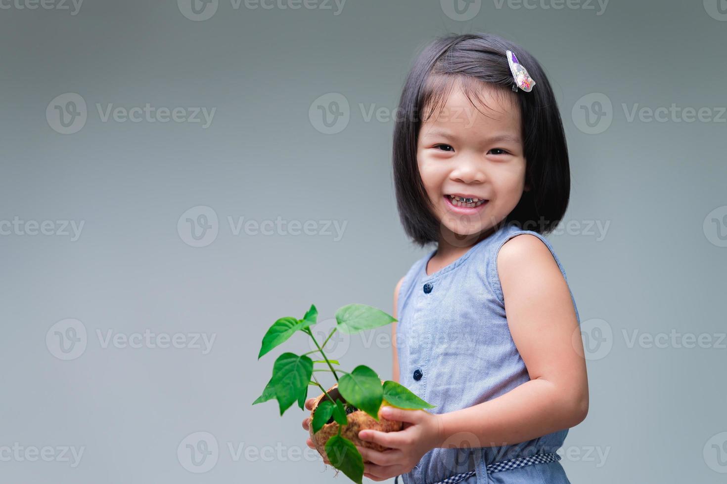 Kind und kleiner Baum im Naturkokosnussschalentopf. süßes Lächeln Mädchen. Welt retten. Umwelt tag. wachsender Baum. Frühling. Umwelt retten. Welttag. Tag der Erde. Kind, das jungen grünen Baum hält. foto