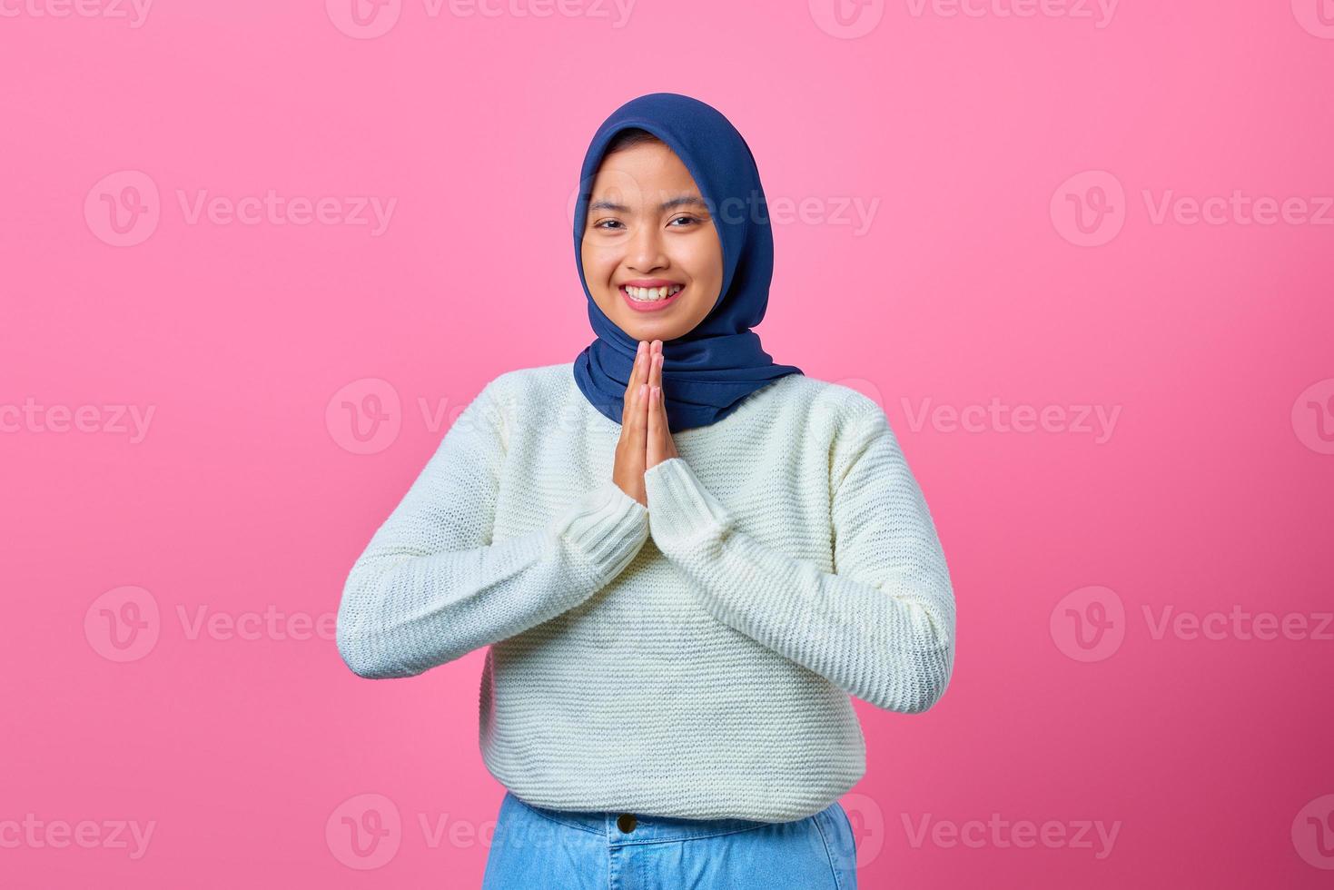 Porträt der lächelnden jungen asiatischen Frau, die betende Geste auf rosa Hintergrund zeigt foto