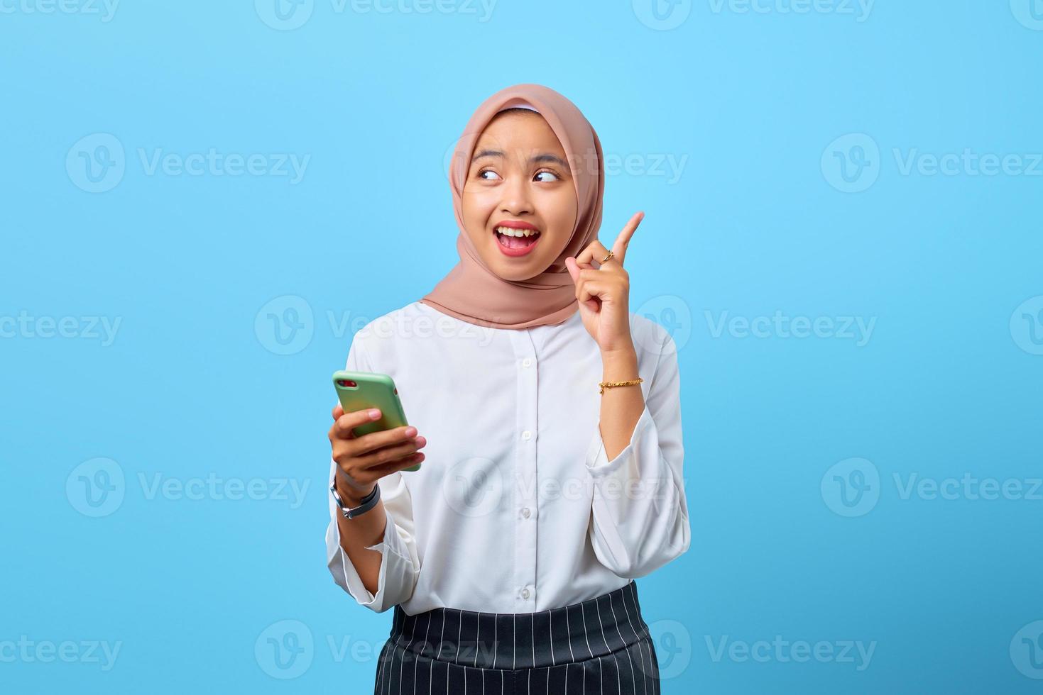 Porträt einer aufgeregten jungen asiatischen Frau, die Handy und erhobenen Finger hält, weil sie Lösungen haben foto