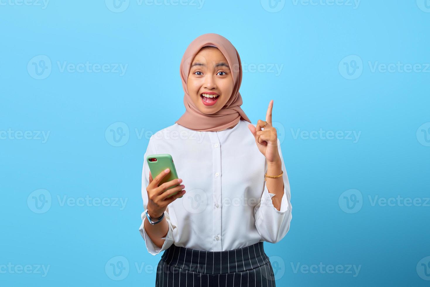 Porträt einer aufgeregten jungen asiatischen Frau, die Handy und erhobenen Finger hält, weil sie Lösungen haben foto