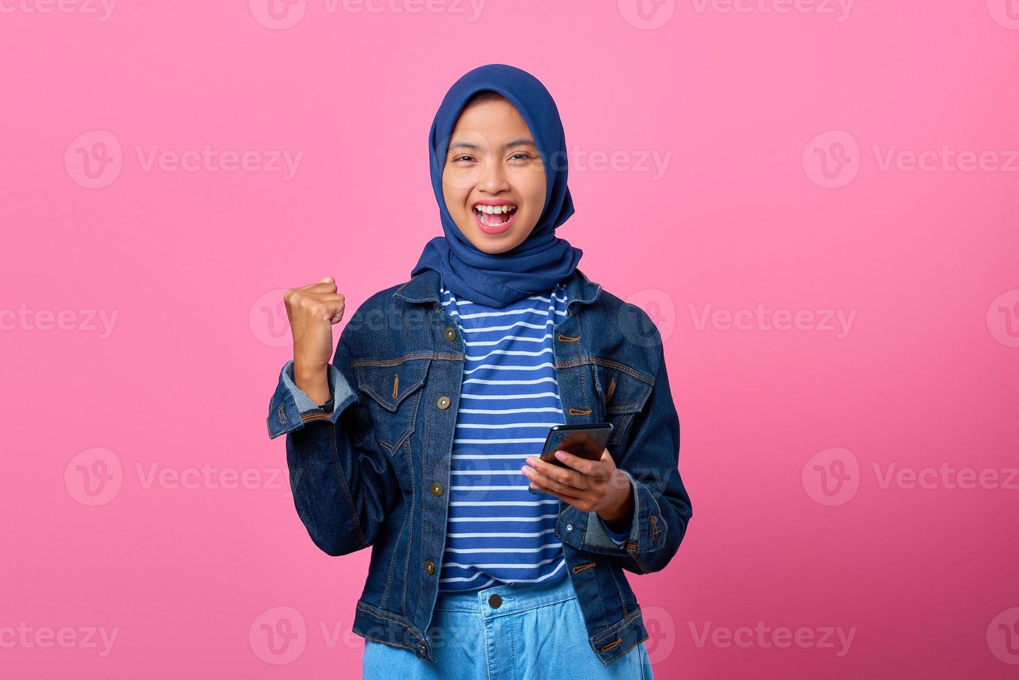 Porträt einer aufgeregten jungen Asiatin, die Smartphone hält und sich freut, den Erfolg zu feiern foto