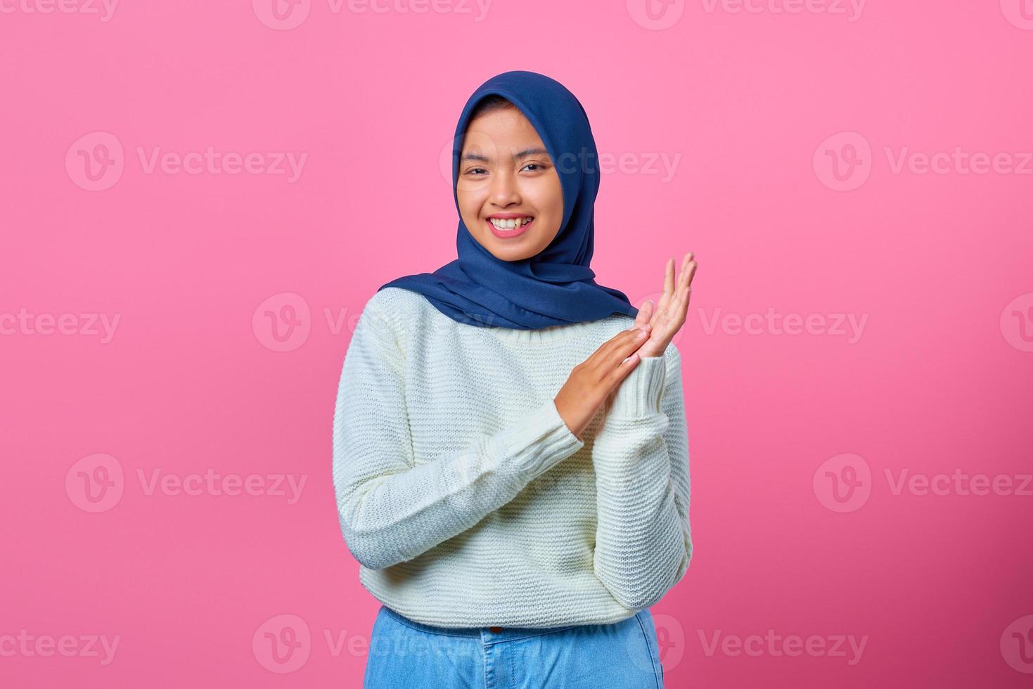Porträt der lächelnden jungen asiatischen Frau, die klatschende Geste auf rosa Hintergrund zeigt foto