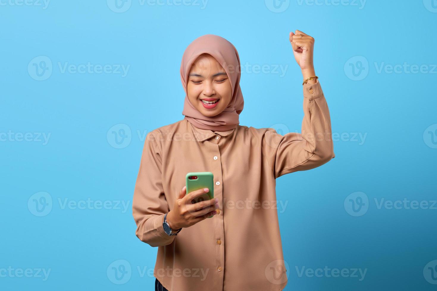 Porträt einer aufgeregten, fröhlichen jungen Asiatin, die das Gewinnen mit dem Handy in der Hand feiert foto