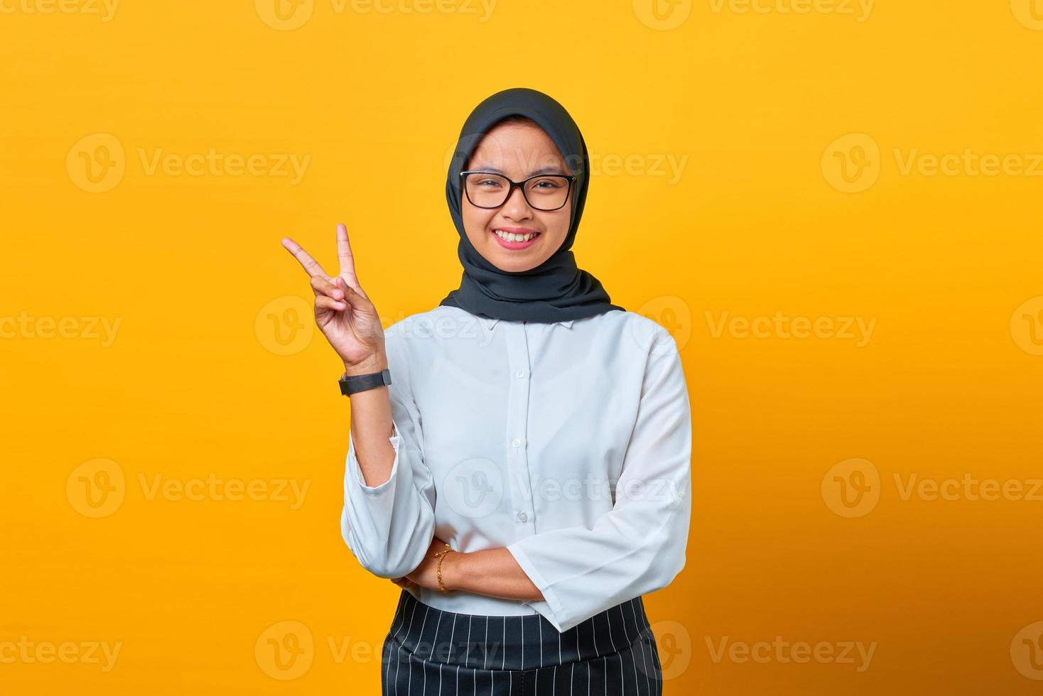 fröhliche junge asiatische frau, die friedenszeichen auf gelbem hintergrund zeigt foto