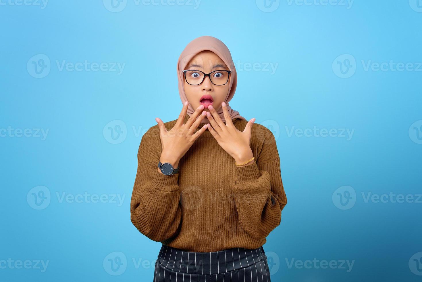 Porträt der überraschten schönen asiatischen Frau mit offenem Mund auf blauem Hintergrund foto