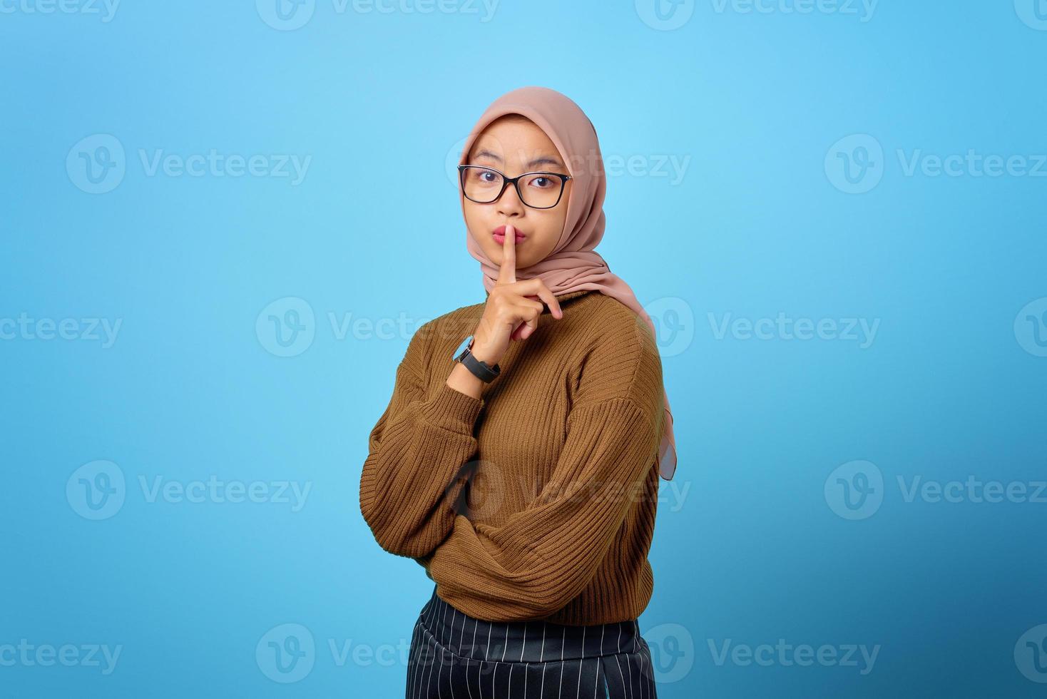 Porträt einer schönen asiatischen Frau, die eine stille Geste auf blauem Hintergrund zeigt foto