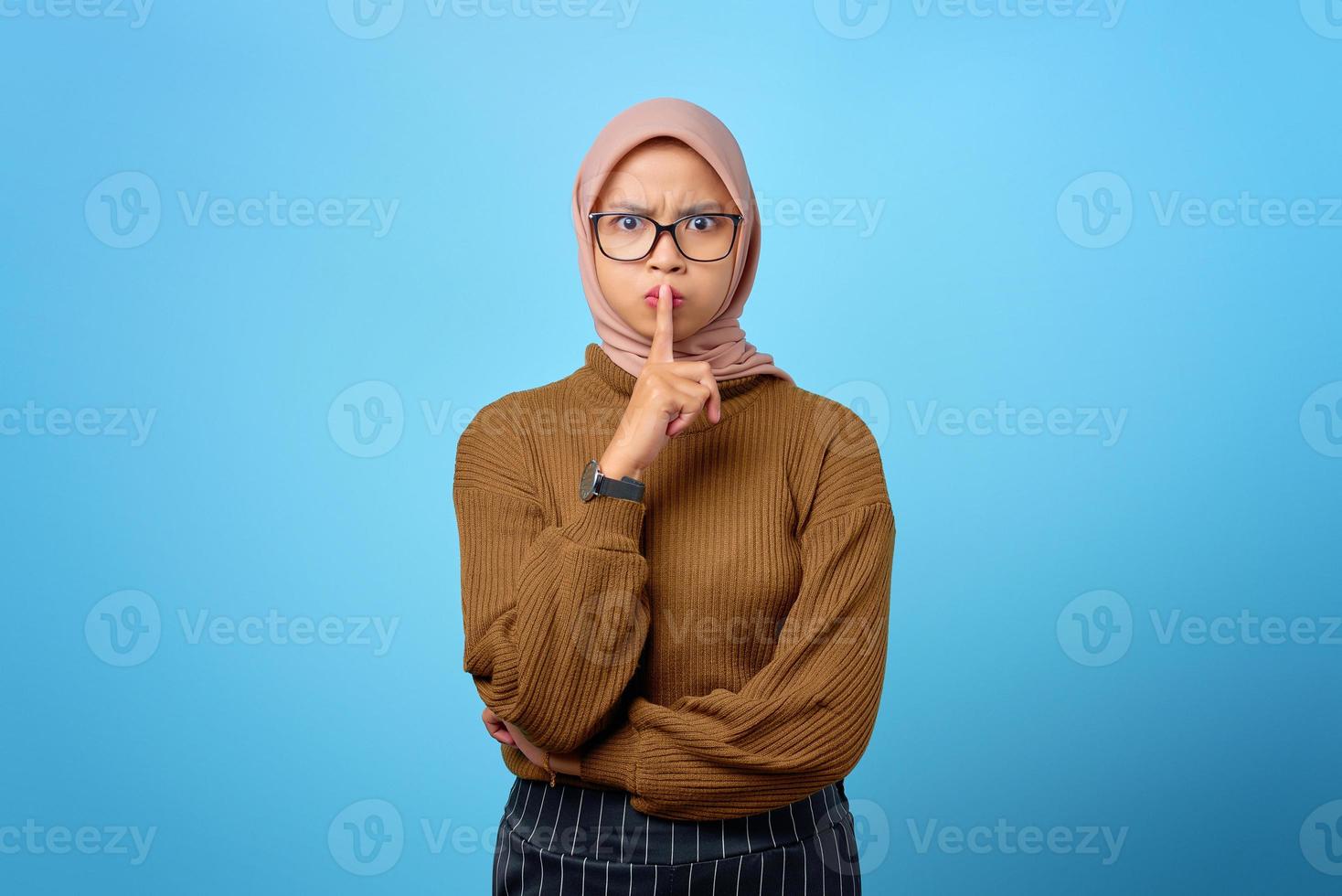 attraktive junge asiatische frau finger auf den lippen und macht eine stille geste auf blauem hintergrund foto