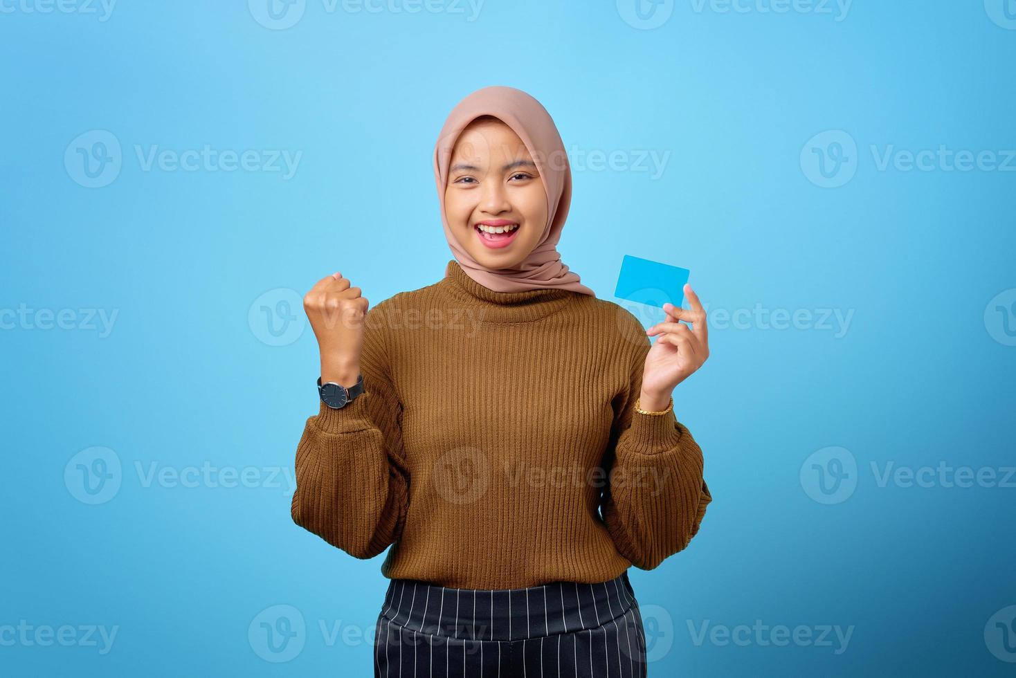 glückliche asiatische frau, die kreditkarte mit handgesteerfolg auf blauem hintergrund hält foto