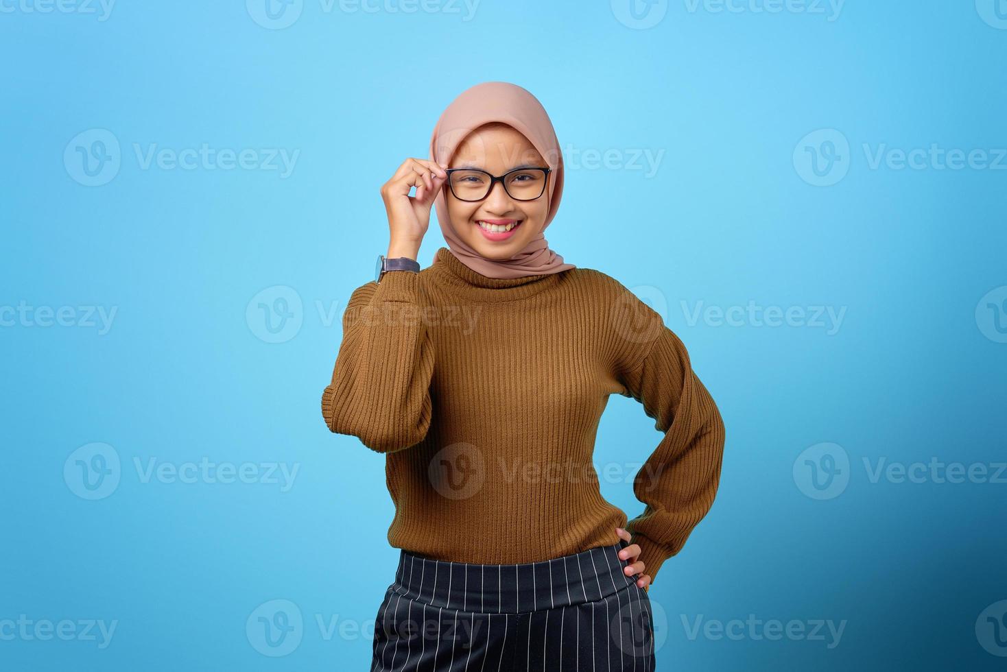 fröhliche junge asiatische frau stehend und berühren brille auf blauem hintergrund foto