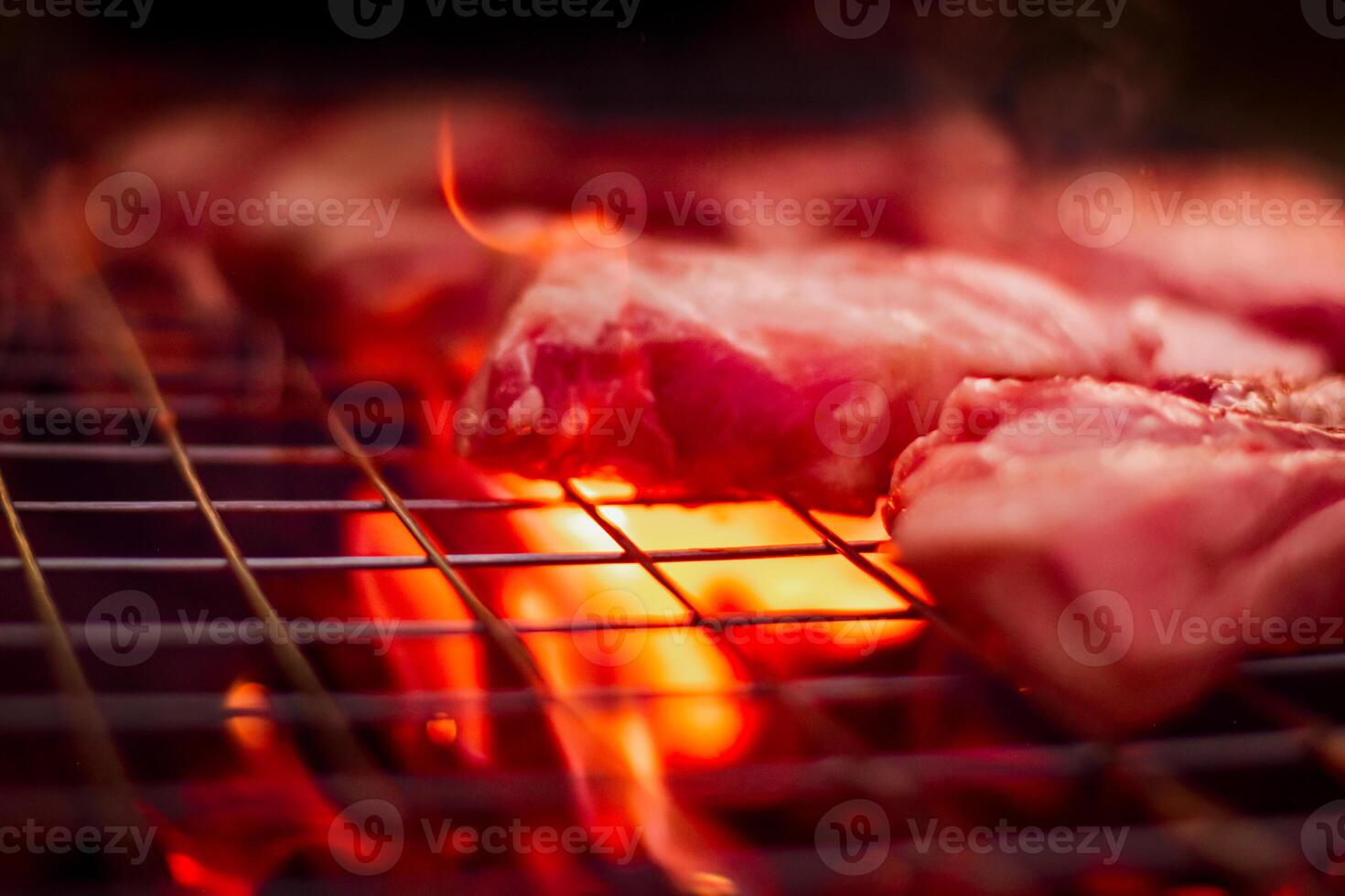 Grillen Schweinefleisch auf rostfrei Stahl Grill mit Flammen auf schwarz Hintergrund, Essen und Küche Konzept. Verbrennung Schweinefleisch auf ein Holzkohle Grill. foto