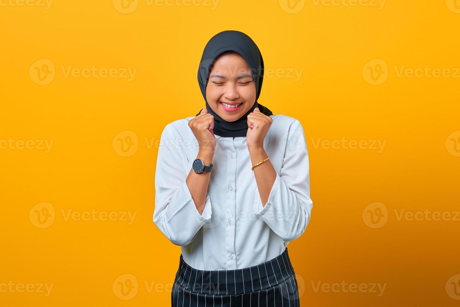 Porträt der aufgeregten schönen asiatischen Frau, die Erfolg auf gelbem Hintergrund feiert foto