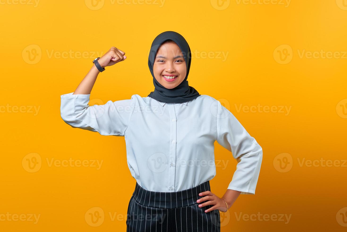 Porträt einer attraktiven jungen asiatischen Frau, die Muskeln auf gelbem Hintergrund zeigt foto