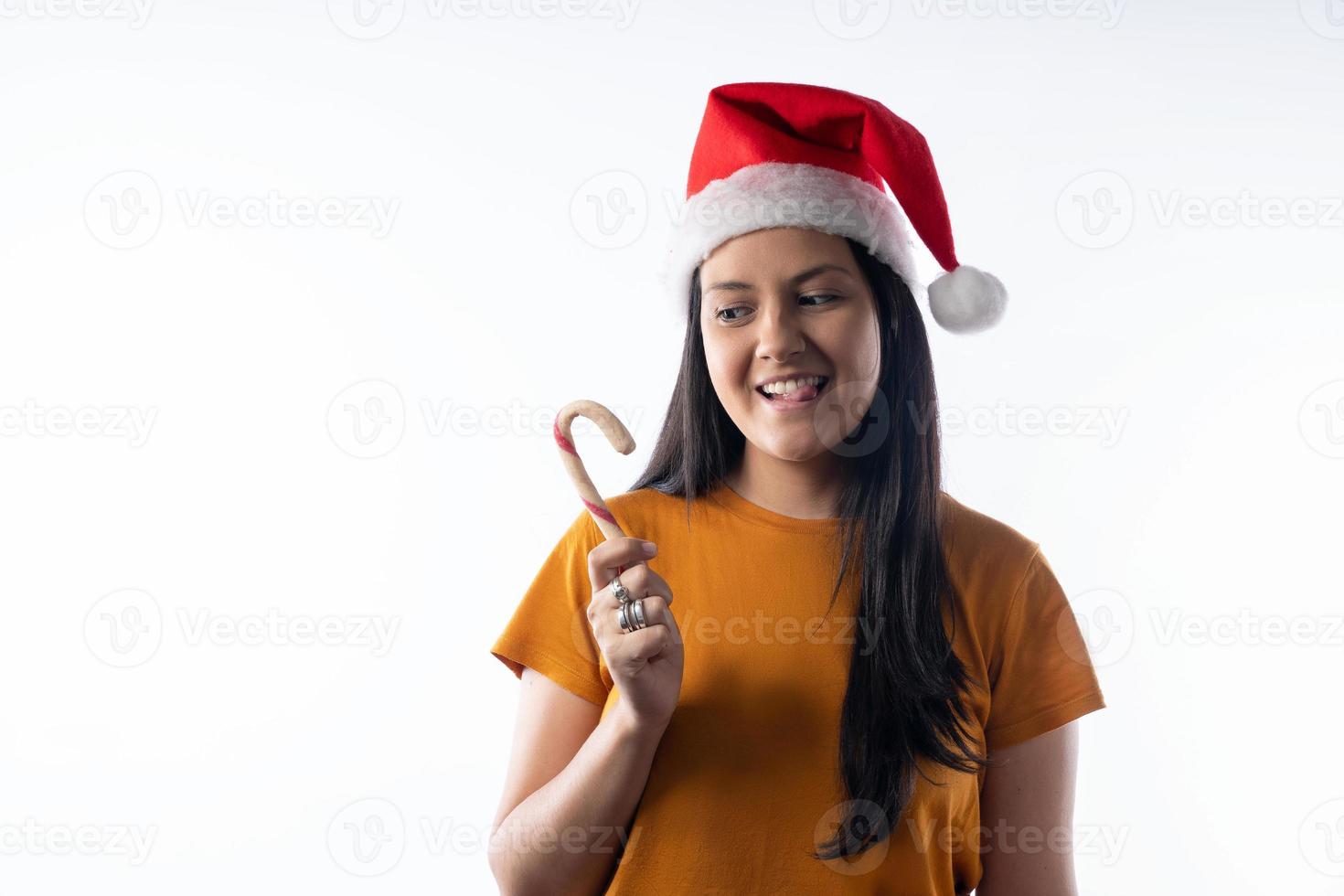 Porträt einer jungen Latina-Frau in Weihnachtsmütze, die sich darauf freut, ihre Weihnachtszuckerstange zu essen. weißer Hintergrund. foto