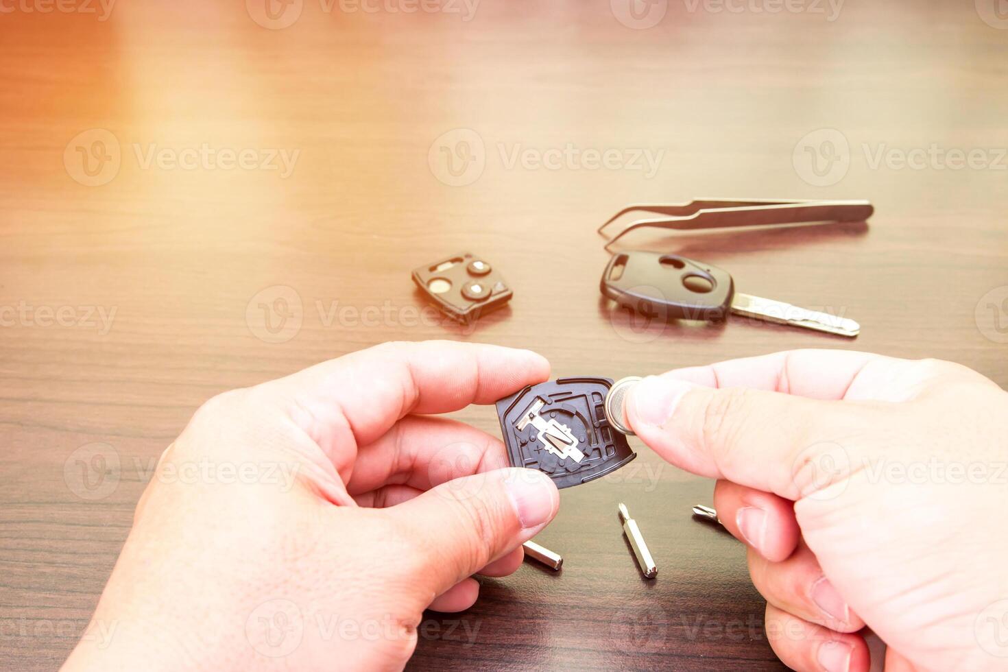 Hand ein Mann Veränderung Batterien von Auto Schlüssel auf Holz Tabelle Hintergrund mit Schraubendreher und Zange mit Sonne Licht foto