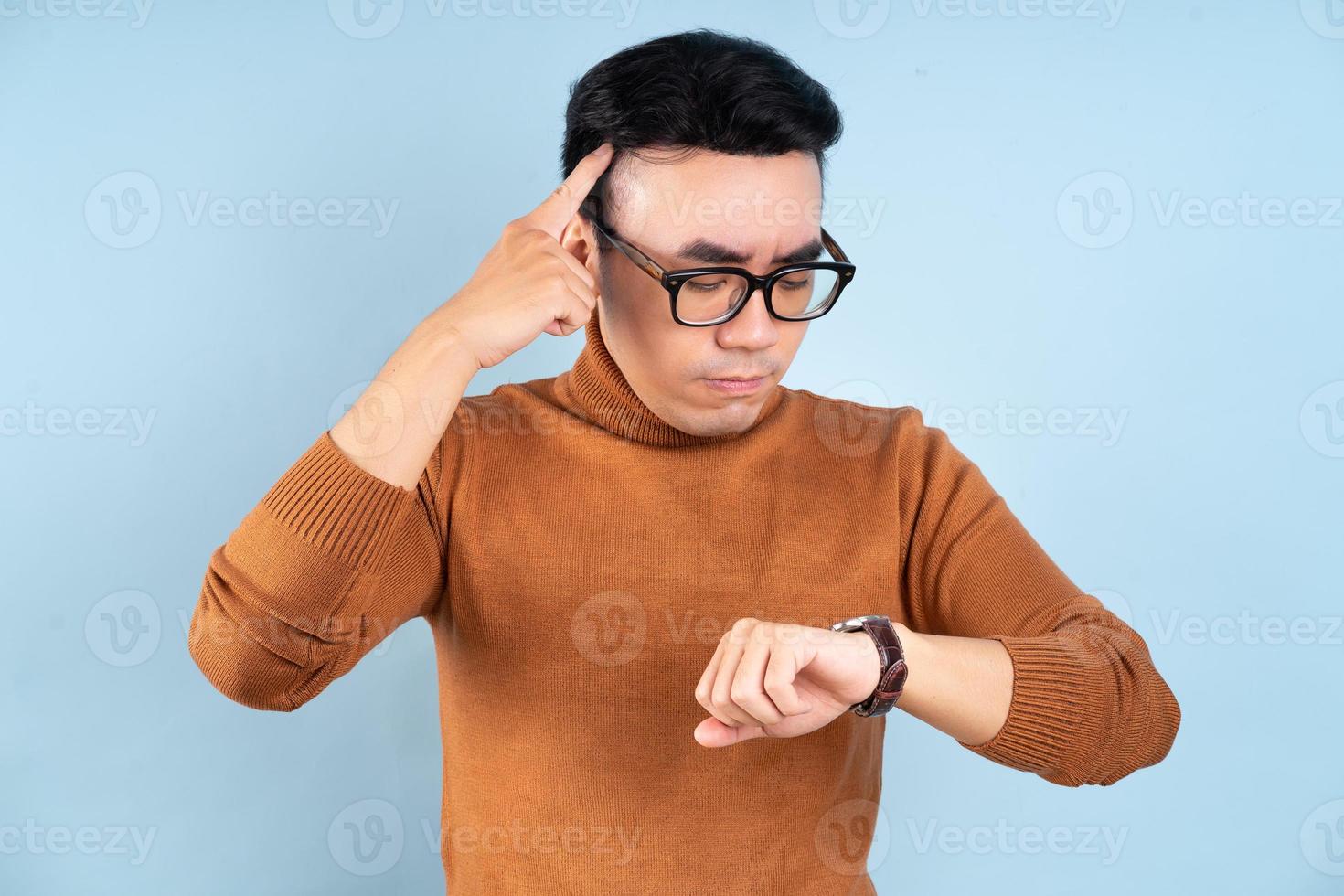 asiatischer Mann, der seine Uhr auf blauem Hintergrund schaut foto