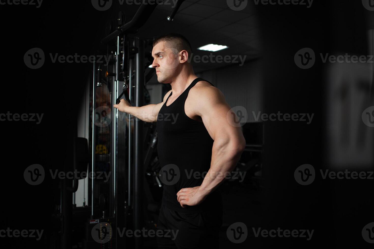 ein Sport Athlet Trainer ein muskulös Mann tut ein Übung auf ein Simulator im Fitnessstudio. Porträt, niedrig Taste, Dunkelheit. ernst foto