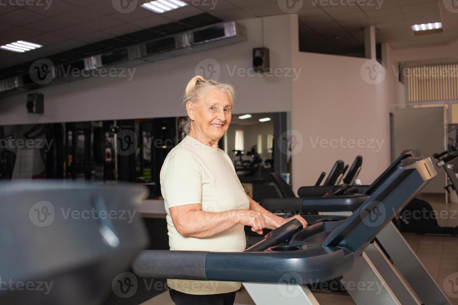 älteste Frau von Pensionierung Alter läuft auf ein Laufband im das Fitnessstudio. Glücklich, lächelnd, Porträt. aktiv, sportlich, gesund Lebensstil im alt Alter. Konzept Senior. modern Technologien. foto