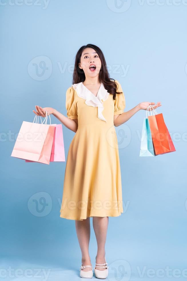 schöne junge asiatische frau mit einkaufstasche auf blauem hintergrund foto