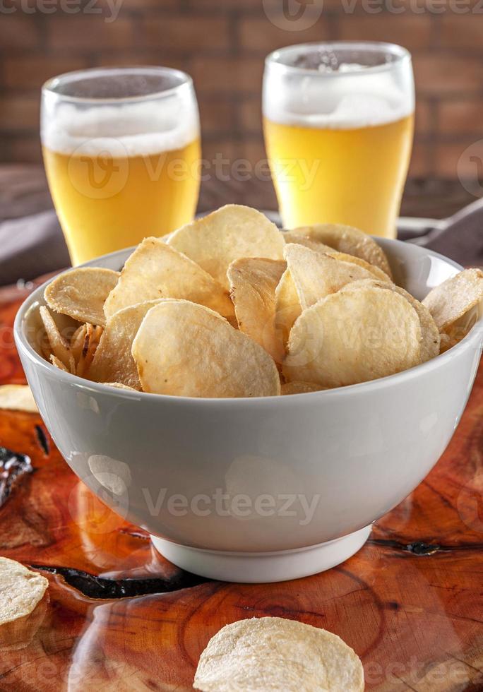 Kartoffelchips in einer Schüssel mit zwei Gläsern Bier foto