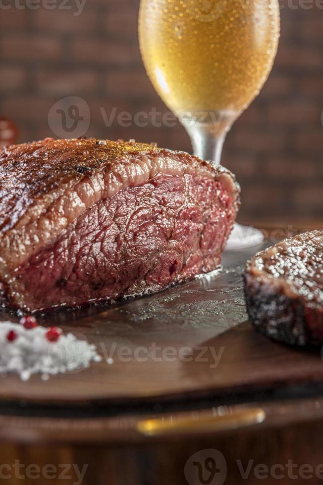 Gegrilltes Rumpsteak in Scheiben geschnitten auf Holzbrett mit einem Glas Bier - brasilianischer Picanha. foto