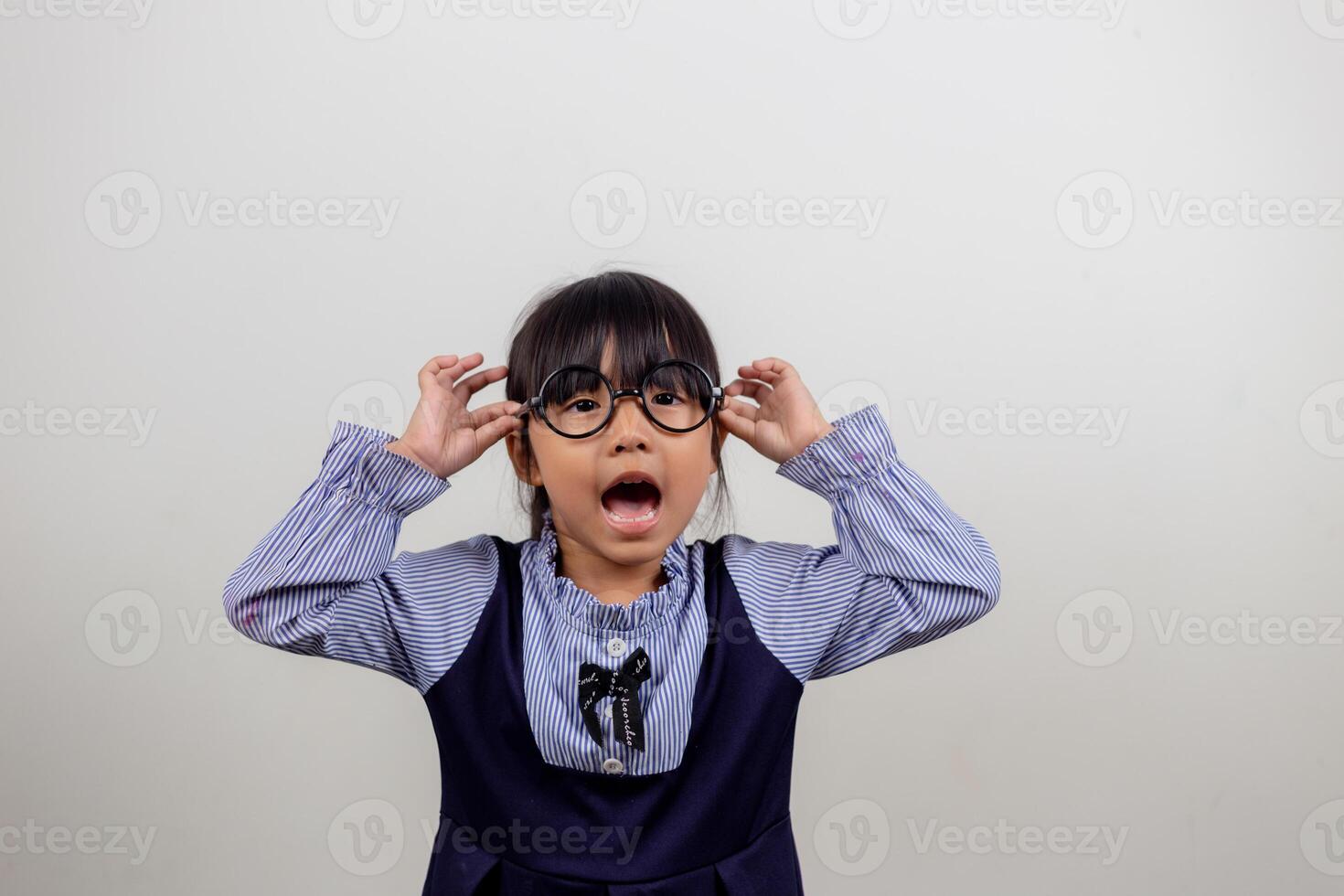 süßes kleines Vorschulmädchen isoliert auf grauem Studiohintergrund trägt eine Brille, schaut in die Kamera, kleines Kind versucht eine Brille bei Optikern, Behandlungskonzept für die Augenkorrektur von Kindern foto