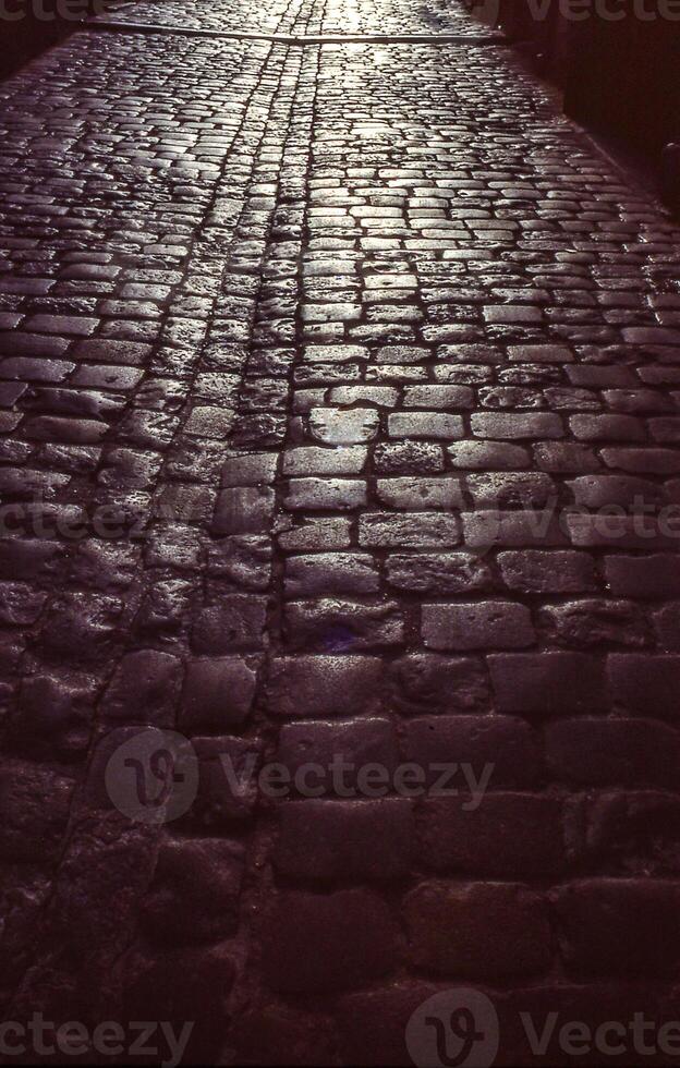 ein Backstein Straße mit ein Uhr Turm im das Hintergrund foto