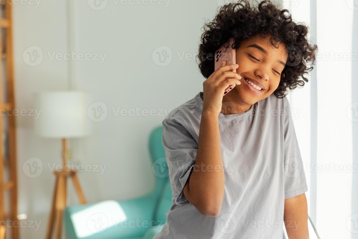 afrikanisch amerikanisch Mädchen reden auf Smartphone beim Zuhause drinnen. jung Frau mit Zelle Telefon chatten mit Freunde. lächelnd Teen Mädchen Herstellung antworten Anruf durch Handy. Dame haben Konversation durch Handy, Mobiltelefon foto
