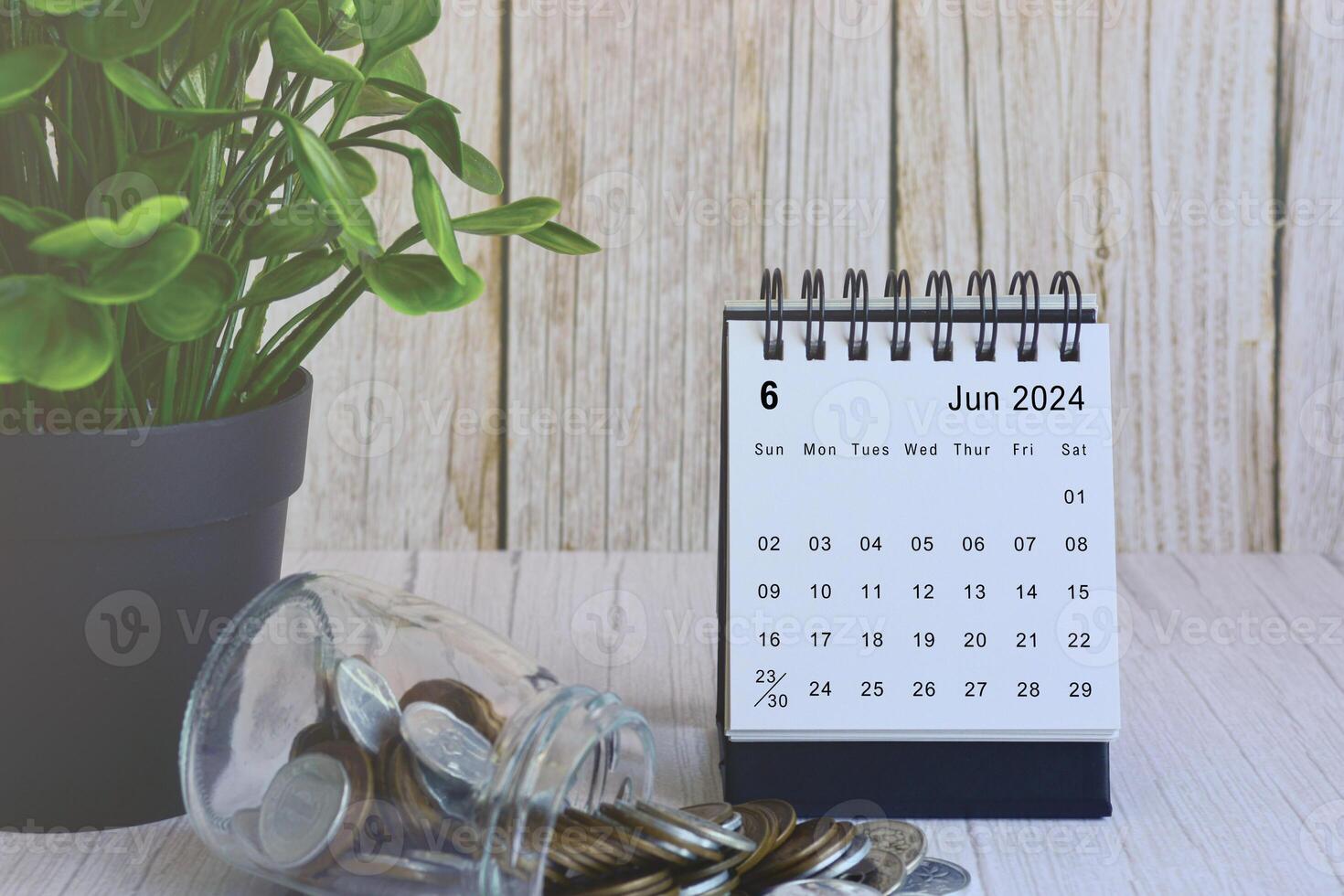 Juni 2024 Schreibtisch Kalender mit Stapel von Münzen und eingetopft Pflanze auf hölzern Schreibtisch. foto