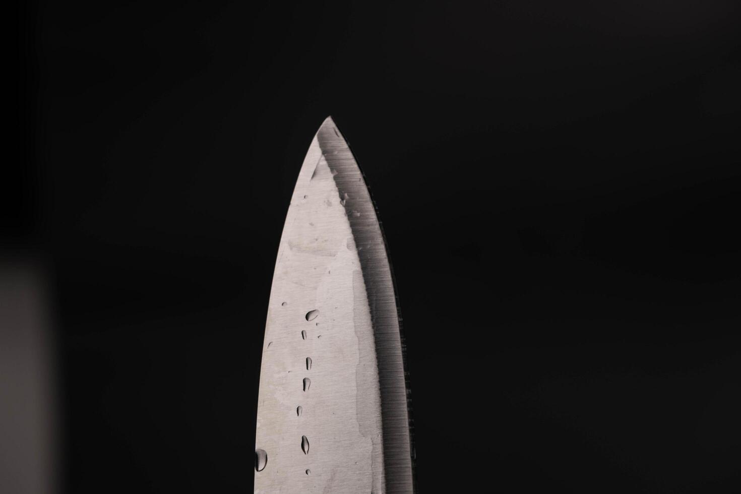 Wasser fallen auf Scharf Messer isoliert auf dunkel Hintergrund. Wasser planschen auf Messer. foto