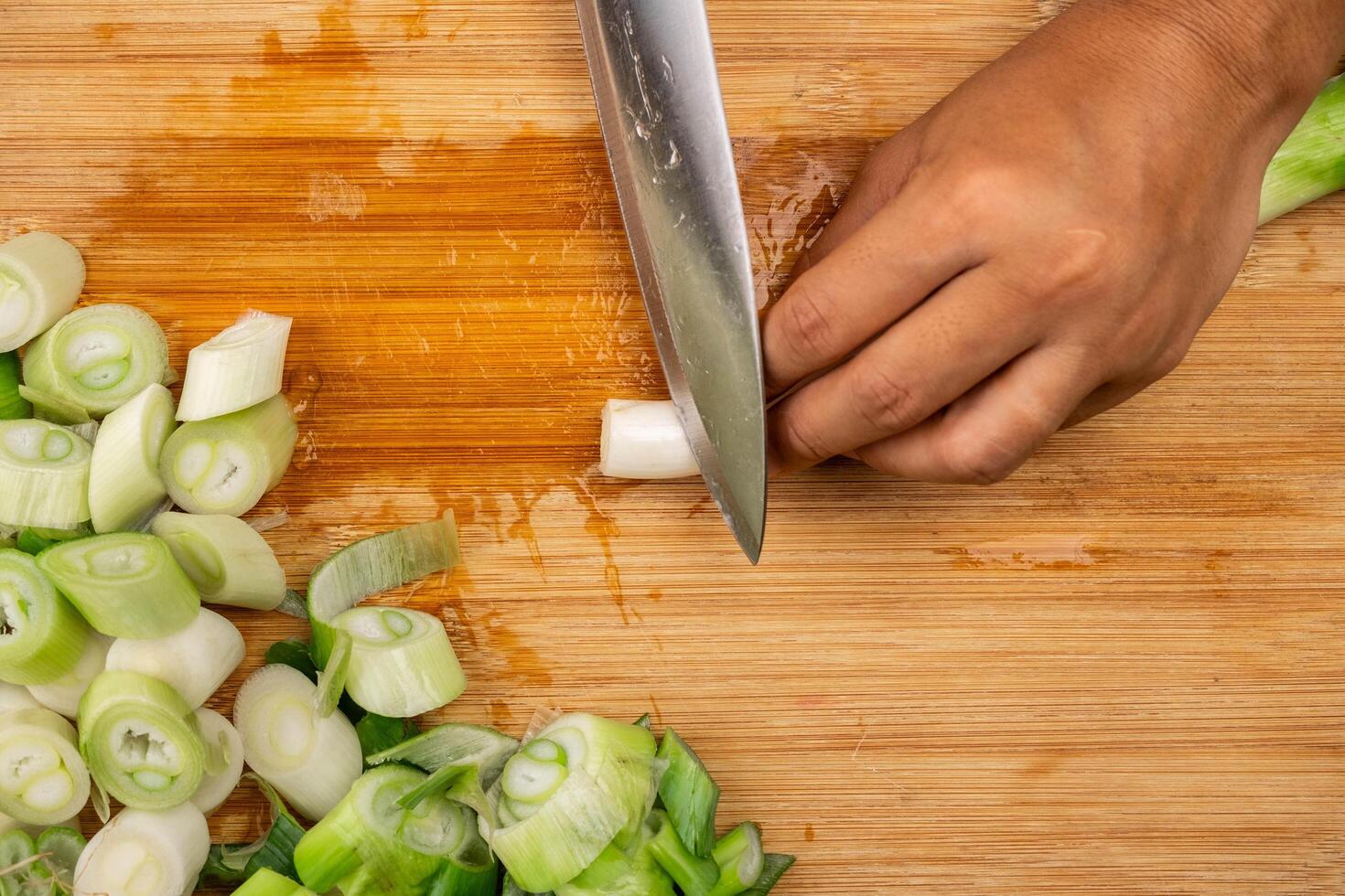 Frau Hand halten ein Messer Schneiden frisch japanisch Frühlingszwiebeln auf ein hölzern Hacken Tafel. geschnitten Lauch oder gehackt Grün japanisch Bündelung Zwiebel auf ein hölzern Tafel. foto