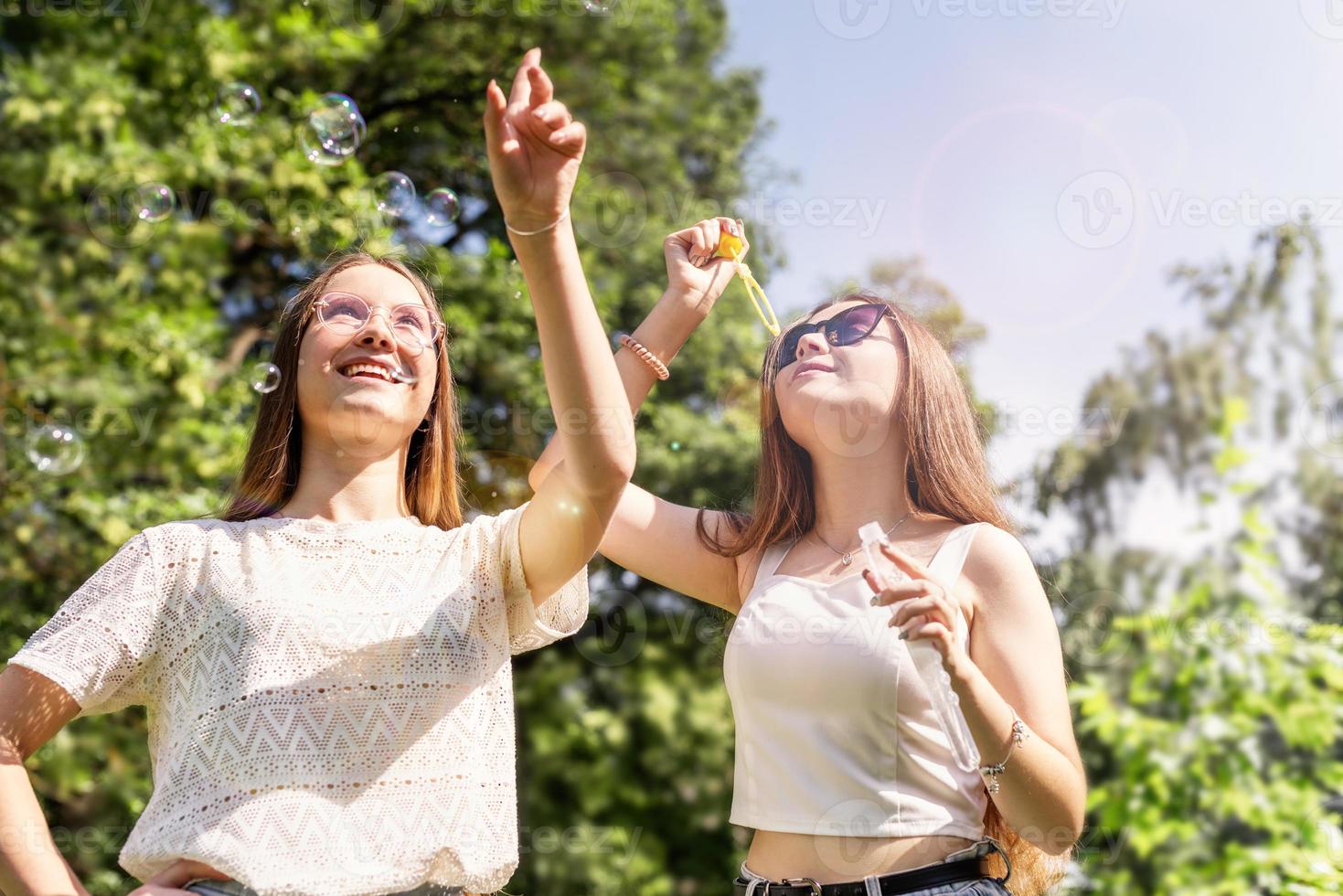 Zwei junge Mädchen, die Seifenblasen blasen und am Sommertag draußen Spaß haben? foto