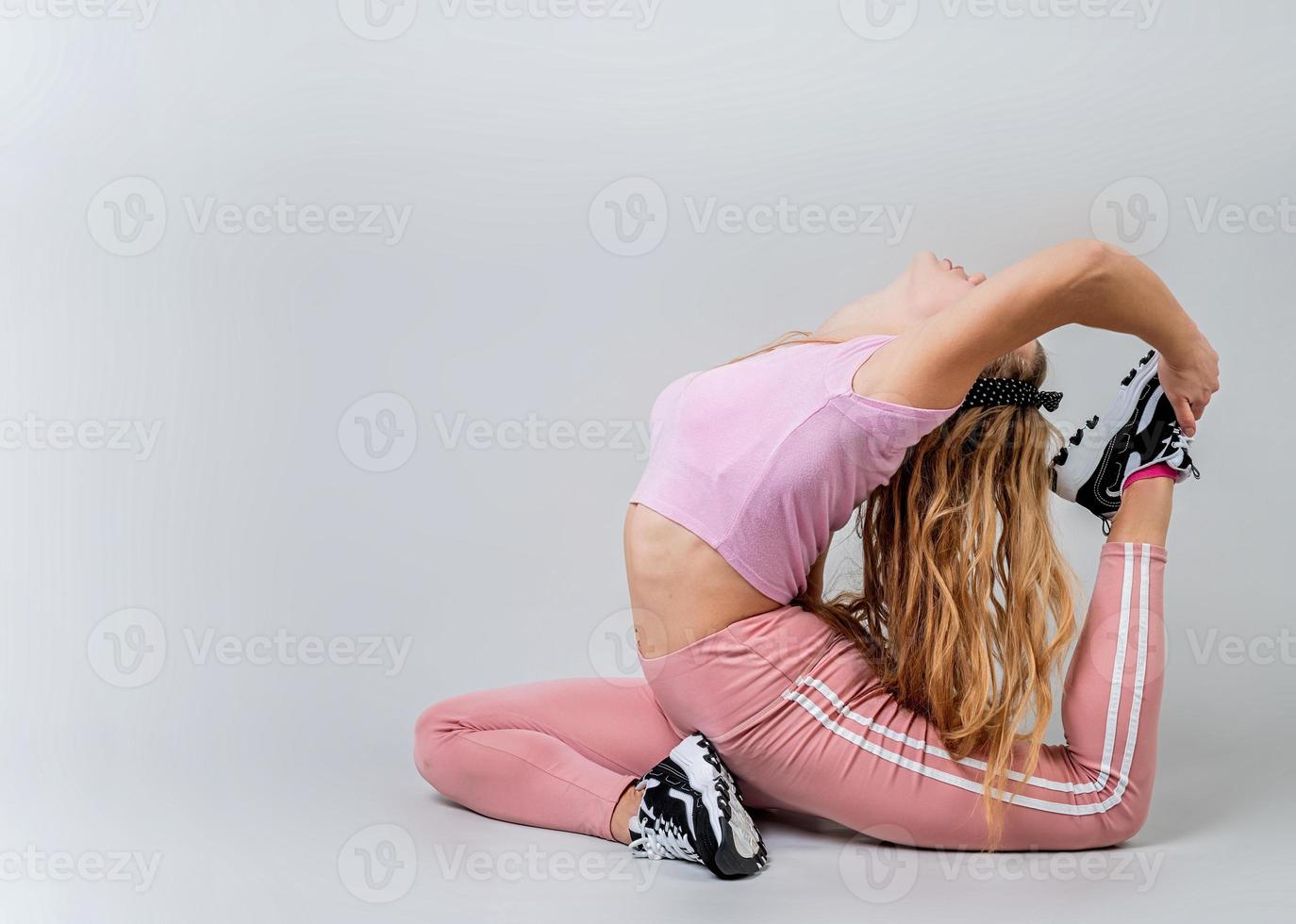 athletische Frau in rosa Sportkleidung beim Yoga im Studio isoliert auf grauem Hintergrund foto