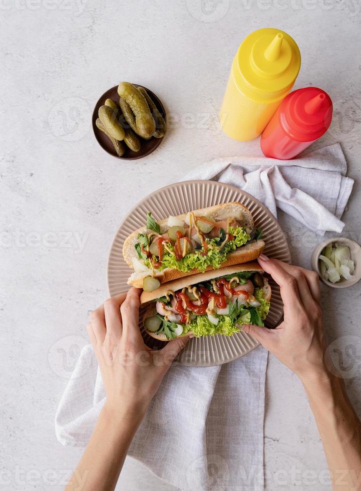 Hot Dog mit Wurst, Salat, Gurke und Zwiebel auf beigem Teller auf Betonhintergrund foto