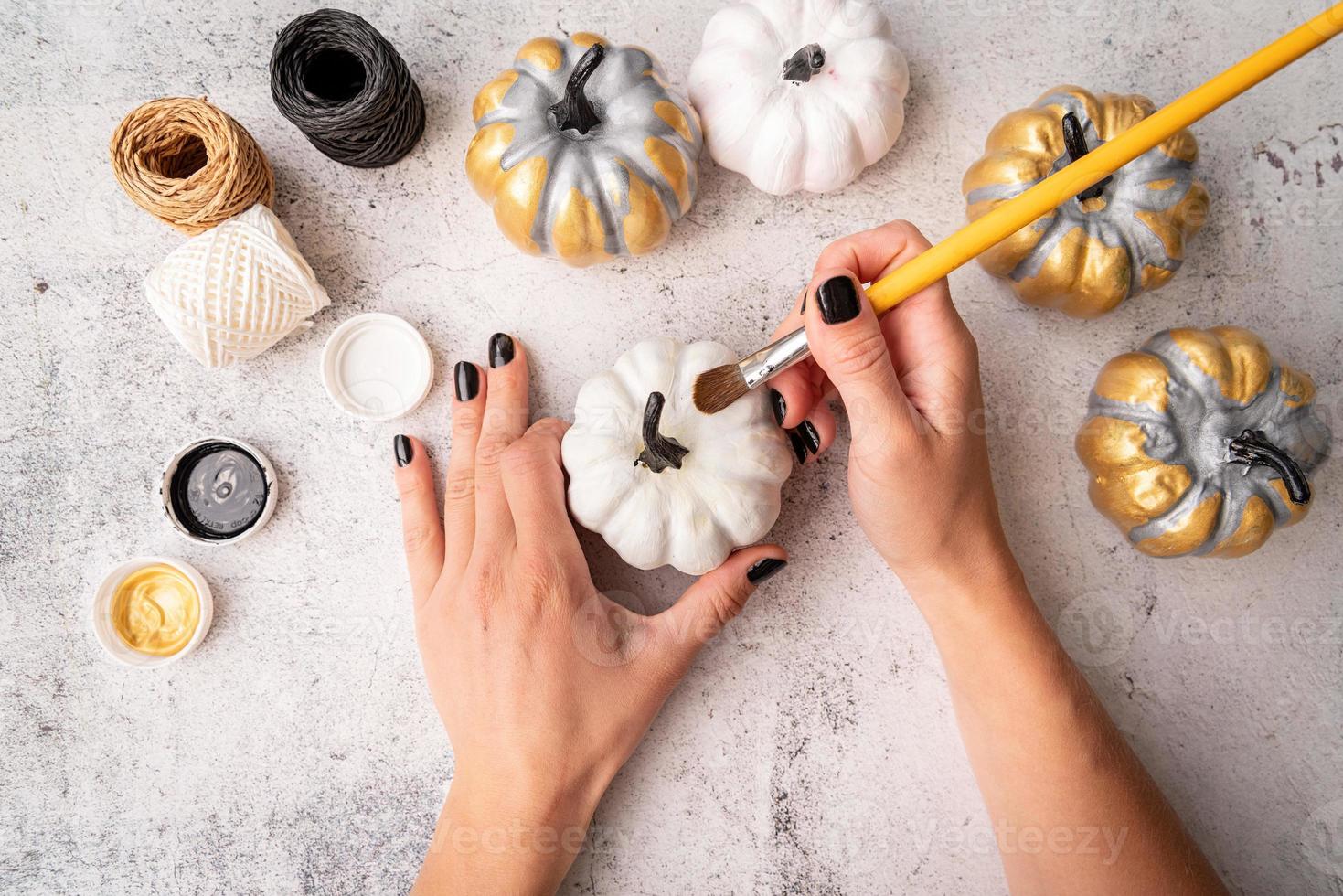 weibliche Hände mit schwarzen Nägeln, die Kürbisse für Halloween malen foto