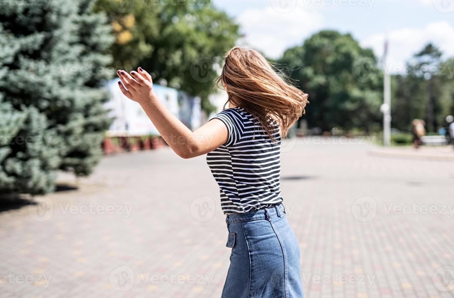 junge hübsche kaukasische Frau in Freizeitkleidung, die Spaß hat, sich auf dem Hintergrund des Stadtparks im Park umzudrehen? foto