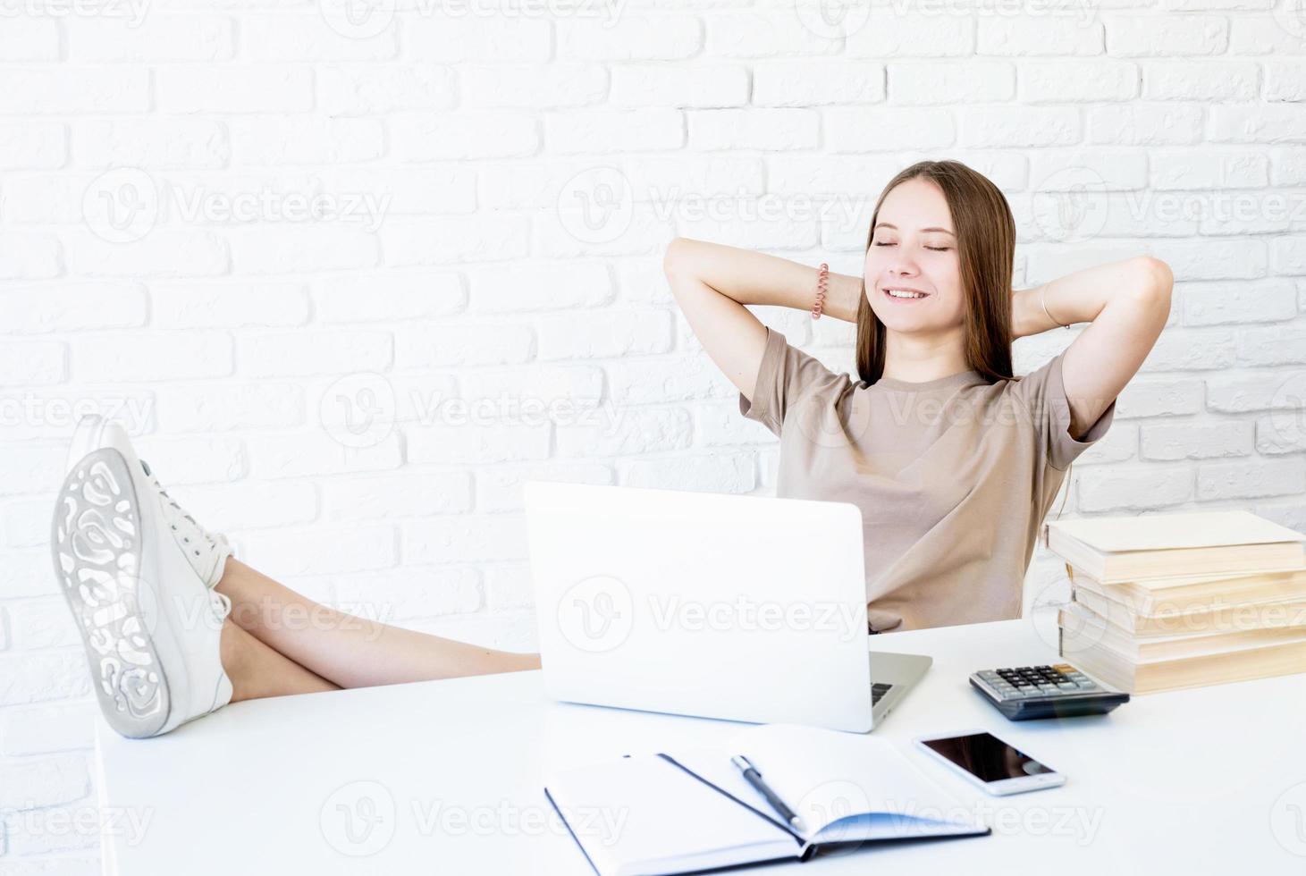 glückliches jugendlich Schulmädchen, das sich vom Studium ausruht und mit den Füßen auf dem Schreibtisch sitzt foto