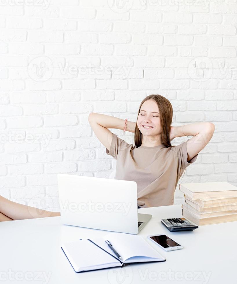 glückliches Teenager-Schulmädchen, das sich vom Studium ausruht und mit den Füßen auf dem Schreibtisch sitzt foto