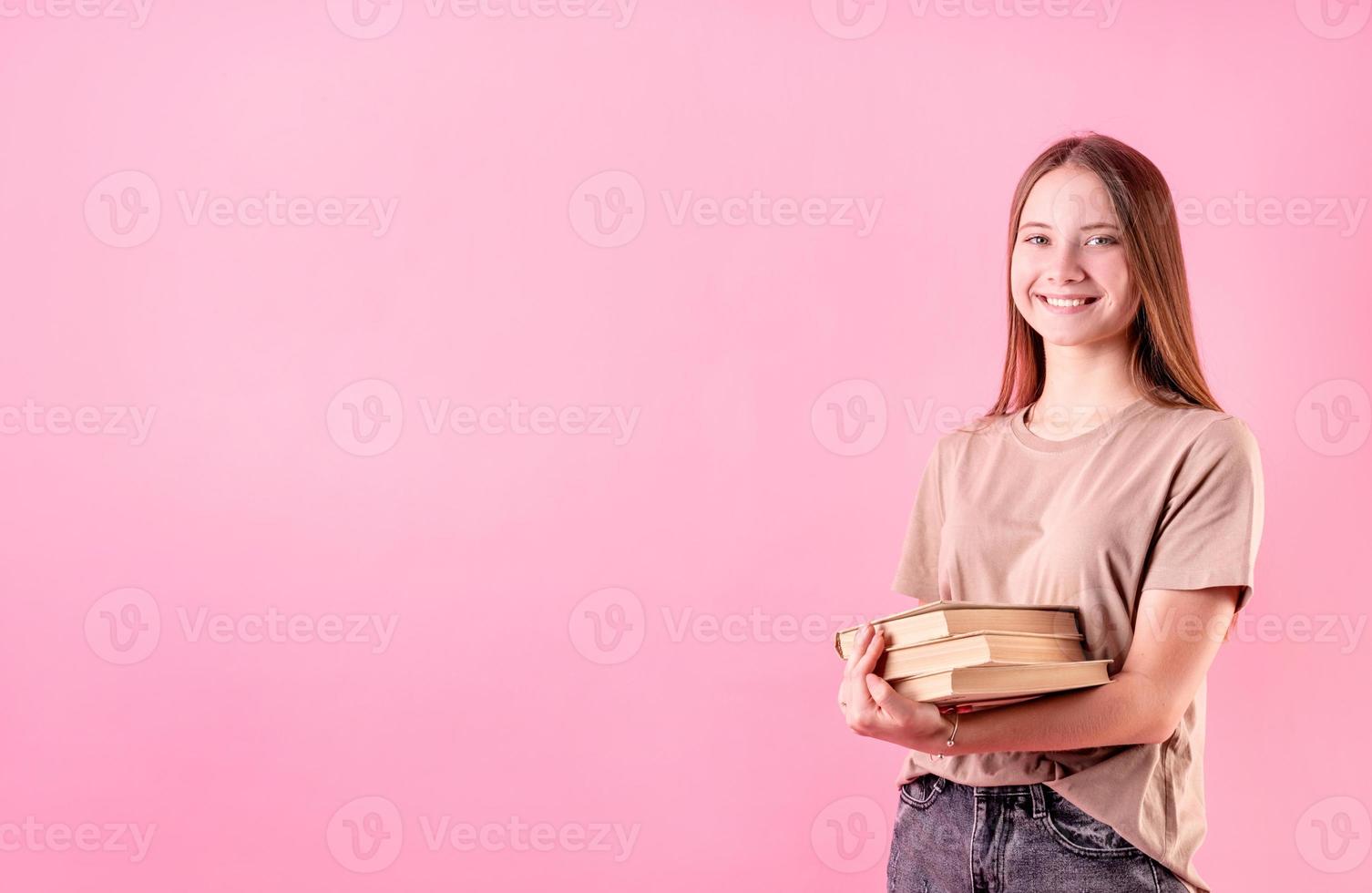 glückliches Teenager-Mädchen, das einen Stapel Bücher auf rosafarbenem Hintergrund hält foto