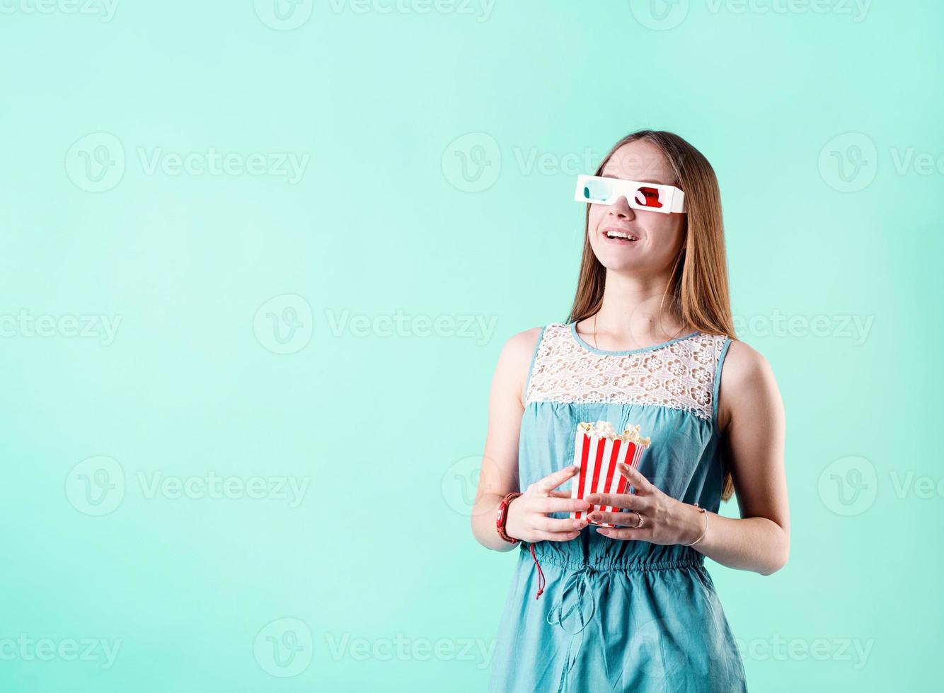 aufgeregt weibliches Teenager-Mädchen mit 3D-Brille isst Popcorn isoliert auf blauem Hintergrund foto