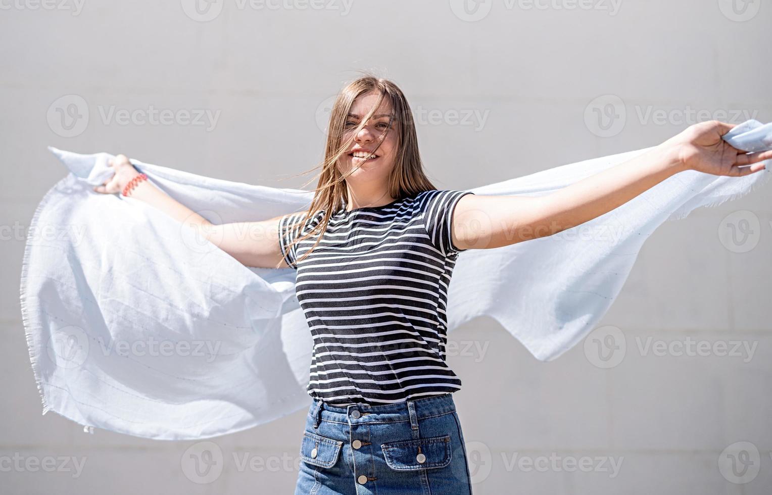 glückliche junge kaukasische Frau mit hellblauem Stoff, die Spaß hat und an einem sonnigen Tag im Sommer im Freien lacht foto