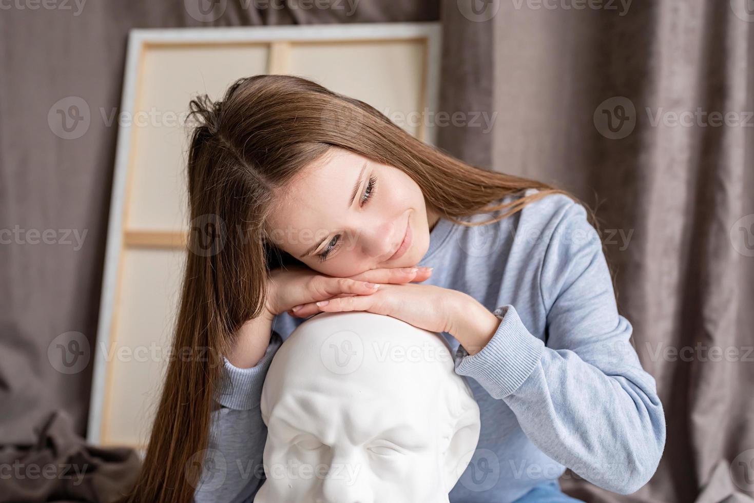 junge Künstlerin sitzt in ihrem Atelier mit dem Kopf aus Leinwand und Gips Sokrates foto