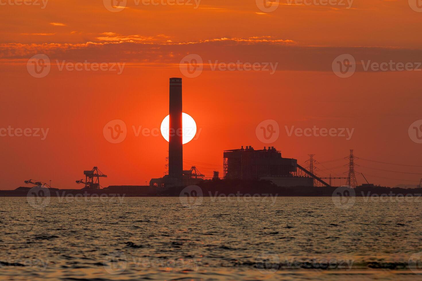 Sonnenuntergang hinter ein industriell Fabrik und im Vorderseite ist das Meer, Orange Farbe, Silhouette foto