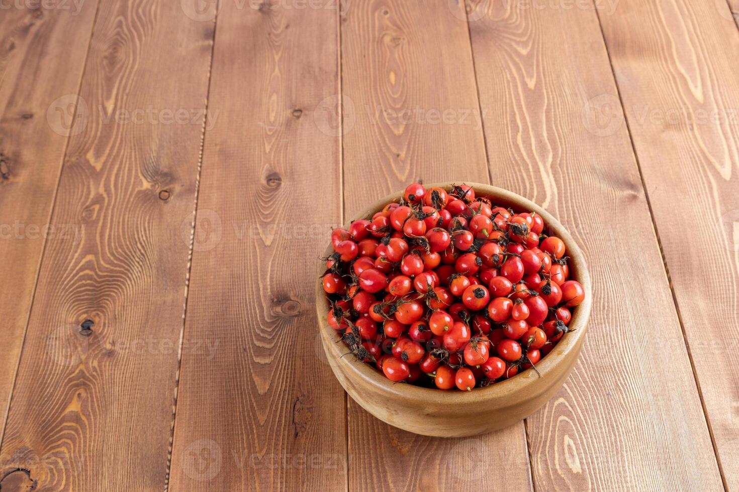 rot Hunderose Hagebutte Früchte im ein hölzern Schüssel auf hölzern Tabelle foto