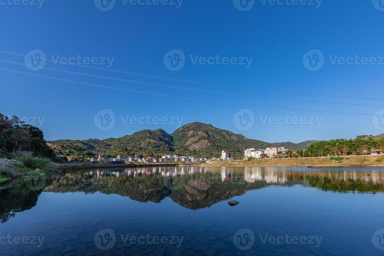 der Landfluss spiegelt den Berg, und die Dörfer und Wälder liegen unter dem blauen Himmel foto